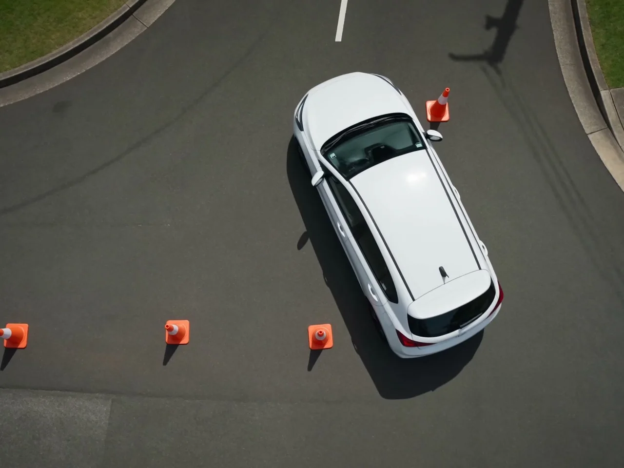 A car reverse parking between three traffic cones on an empty stretch of bitumen, seen from above