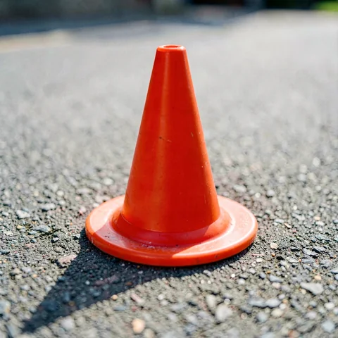 A single traffic cone on grey bitumen with a long low-angle shadow